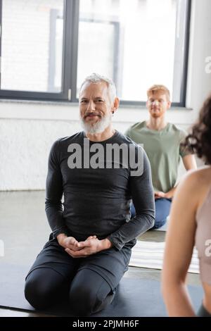 Smiling middle aged man looking at camera while practicing yoga in Thunderbolt asana in studio,stock image Stock Photo