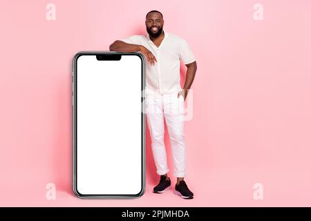 Full body photo of cheerful man standing near huge empty space phone isolated on pink color background Stock Photo