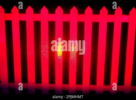Semiabstract picture of a vivid red coloured picket fence isolated against a dark black background Stock Photo