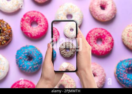 Woman taking picture of delicious doughnuts on violet background, top view Stock Photo