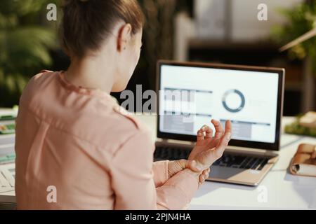 Seen from behind modern business woman with laptop having wrist pain in modern office. Stock Photo