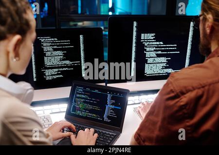 Close-up of two young developers working over data decoding software while young female IT engineer typing on laptop keyboard Stock Photo