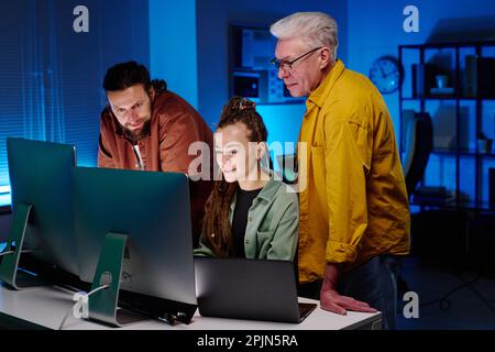Group of IT engineers looking at screen of desktop computer at working meeting while young smiling woman making presentation Stock Photo