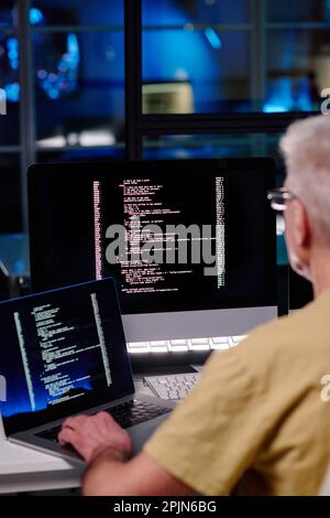 Close-up of experienced male IT engineer using new software for decoding data while sitting by workplace in front of computer screens Stock Photo