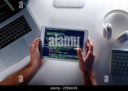 Top view of tablet screen with coded data held by male programmer using or creating new software while sitting by workplace in office Stock Photo