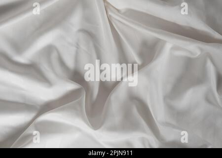Satin crumpled fabric of white color, top view. Natural bed linen, sheets, abstract background of luxury fabric, wavy folds Stock Photo