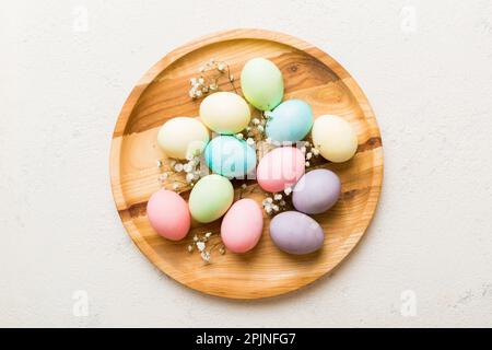 Happy Easter composition. Easter eggs in basket on colored table with gypsophila. Natural dyed colorful eggs background top view with copy space. Stock Photo