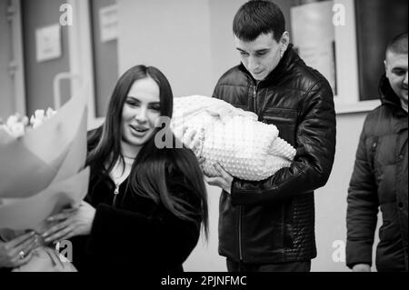 A man holds a baby wrapped in a blanket next to a beautiful women who holds flowers Stock Photo