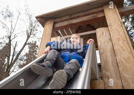 Cute little boy with blonde hair playing in the slider at the playground Stock Photo