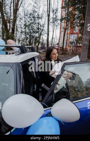 A beautiful woman stands near a car and holds a baby wrapped in a blanket Stock Photo