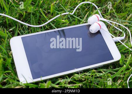 White smartphone and headphones, on the green grass Stock Photo