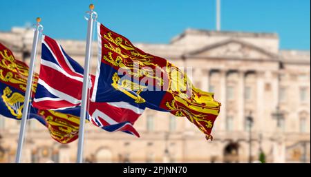 The Royal Standard of the United Kingdom waving with the UK flag with blurred Buckingham Palace in the background. 3d illustration render. rippled tex Stock Photo