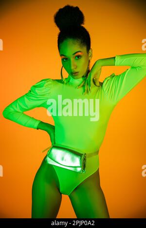Stylish african american model with neon makeup and bodysuit standing on orange background,stock image Stock Photo