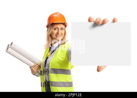 Smiling female engineer with a safety vest and hardhat holding blueprints and showing a blank card isolated on white background Stock Photo