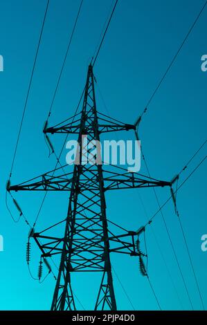 High voltage electric tower silhouette on bright blue background. Stock Photo
