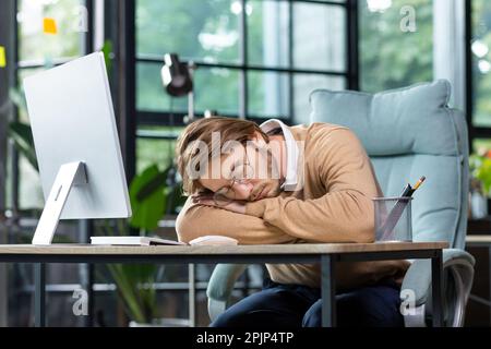Tired programmer, IT specialist fell asleep at the workplace in the office, at home on the table in front of the computer. Overtime, deadline, project. Stock Photo
