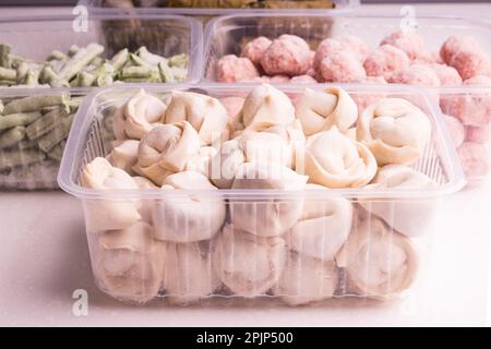 Frozen vegetables and semi-finished meat products in plastic containers on a white plate. meatballs, dumplings, chopped beans Stock Photo