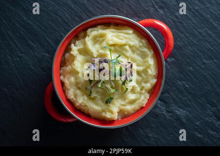 Mashed potatoes with radish microgreens in a red saucepan close up, top view Stock Photo