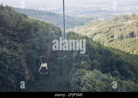 Cable car go to top of mountain among trees in forest on summer sunny day. Panoramic view of valley at mountain Stock Photo