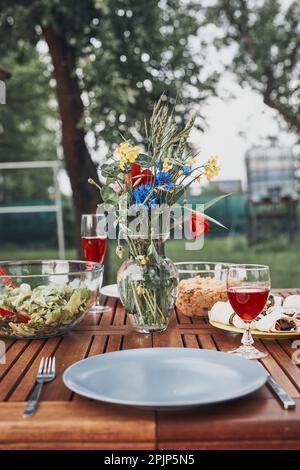 Dinner in an apple orchard garden on wooden table with salads and wine decorated with flowers. Close up of table with food prepared for family dinner Stock Photo