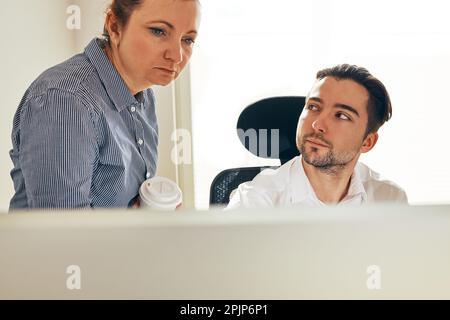 Two business people discussing financial data looking at computer screen. Businesswoman talking to young male coworker in office. People entrepreneurs Stock Photo