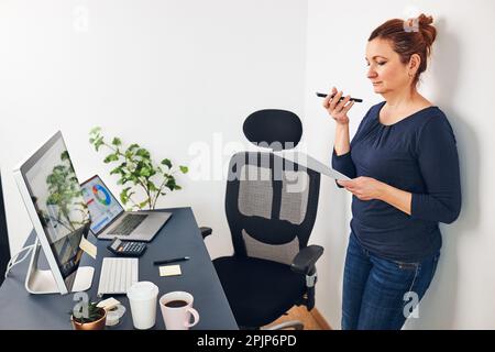 Woman entrepreneur having business  conversation on mobile phone. Businesswoman working in office holding documents and smartphone. Woman standing by Stock Photo