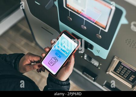 Woman buying ticket at ticket machine paying using mobile payment app on smartphone. Female buying bus public transport ticket in vending machine Stock Photo