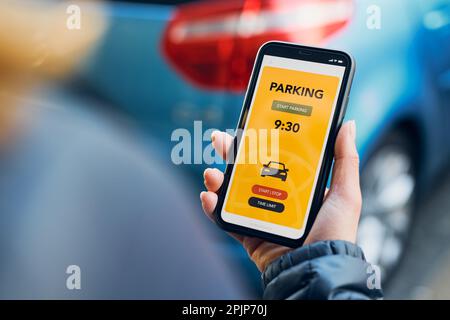 Woman using mobile parking app on smartphone. Driver using smartphone to pay for parking. Car park application on mobile phone. Convenience paying Stock Photo