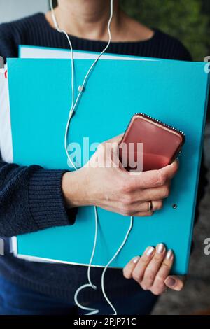Woman working remotely doing job during call conversation on phone from home. Woman holding smartphone and documents in binder using headphones Stock Photo
