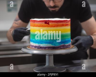 pastry chef working on a frosted cup cake with lgbt rainbow colours for wedding union party celebration. Birthday cupcake. Rainbow paper cup liners. H Stock Photo
