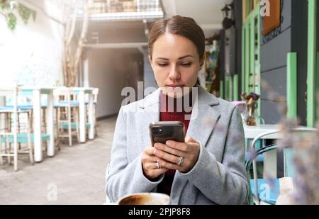 Woman texting using her mobile phone wile sitting in outdoor cafe. Stock Photo