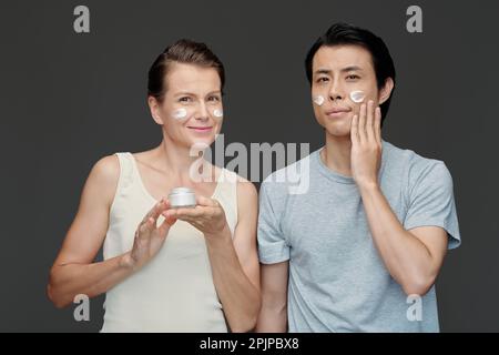 Portrait of smiling man and woman applying face cream Stock Photo