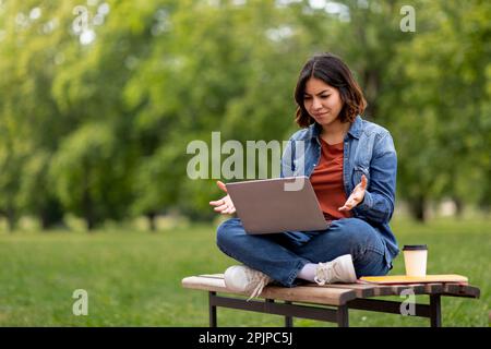 Confused Arab Woman Having Problem With Laptop While Sitting On Bench Outdoors Stock Photo