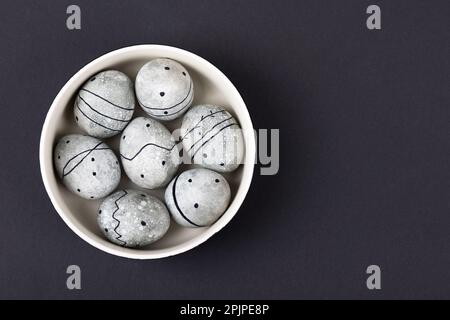 Seven grey Easter eggs in a black pattern in a bowl on a black background. Happy Easter concept. Stock Photo