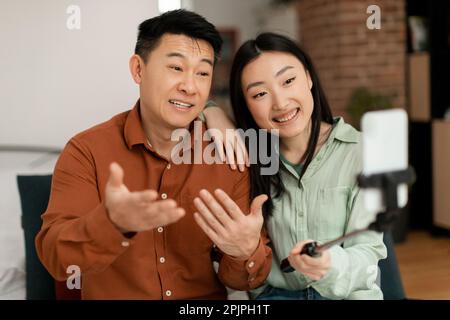 Happy asian man and woman having video call with family, talking and gesturing at cellphone webcamera Stock Photo