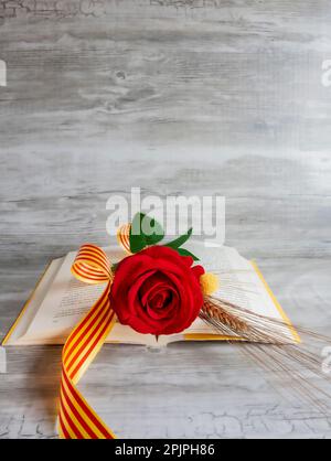 Rose and yellow book, ear of wheat, with Catalan flag and red ribbon, on beige background with texture, vertical, copy space, valentine’s day Stock Photo