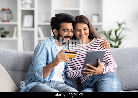 Happy young interracial couple using bank card, digital tablet Stock Photo