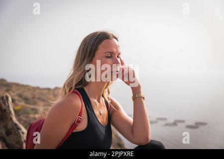 A woman takes a break while hiking and meditates sitting on a rock. Stock Photo