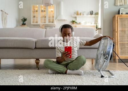 African American child boy relaxing with smartphone in front of electric fan at home.  Stock Photo