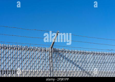Barbed wire topper on a chain link fence with slats Stock Photo