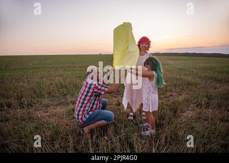 Diversity family, mother father daughter light a yellow paper lantern in the sky at sunset in the field. Teamwork. Making wishes. Concept of hope, fai Stock Photo