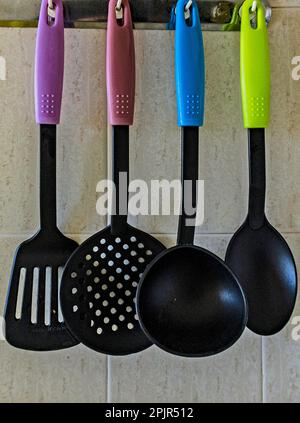 Four colourful kitchen utensils hanging on a kitchen wall. Stock Photo