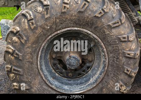 Black rubber tire covered with dried mud on All Terrain Vehicle parked on gravel surface. Stock Photo