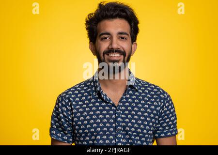 Portrait of happy calm indian man smiling friendly, glad expression looking away dreaming resting, relaxation feel satisfied concept good news, celebrate win. Hindu guy on studio yellow background Stock Photo