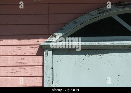 old, weathered clapboard siding and decorative portal with rounded window above Stock Photo