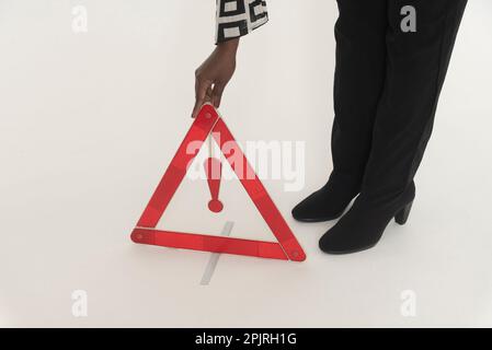 England, UK. 2022.  Woman driver placing a red danger triangle to warn oncoming traffic of  a motoring situation ahead, Stock Photo