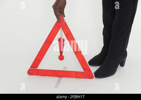 England, UK. 2022.  Woman driver placing a red danger triangle to warn oncoming traffic of  a motoring situation ahead, Stock Photo