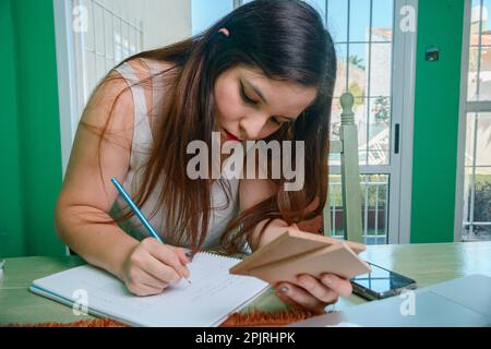 young latin woman of argentinian ethnicity, interior designer leaning on table making blueprints writing on notebook with graphite pencil, holding woo Stock Photo