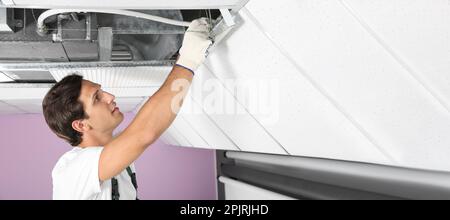 Young male technician repairing air conditioner indoors, space for text. Banner design Stock Photo