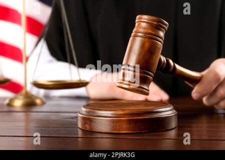 Judge with gavel at wooden table near American flag, closeup. Space for text Stock Photo